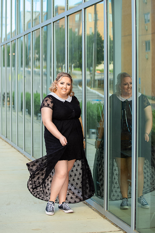 Oak Ridge High School senior in black lace dress poses against modern glass building in Huntsville Texas with artistic reflections Amanda Holloway Photography location.